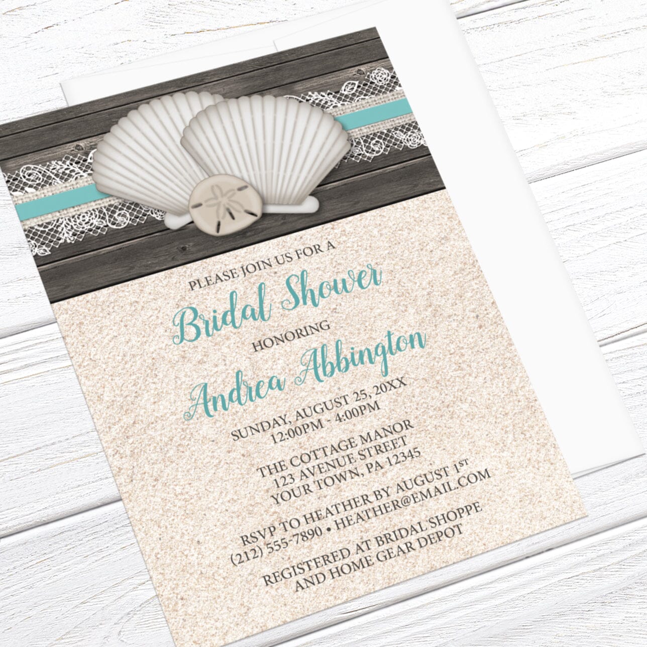 Beach-themed bridal shower invitation with shells, lace, wood, and sand, displayed at an angle view with an envelope on a wooden background