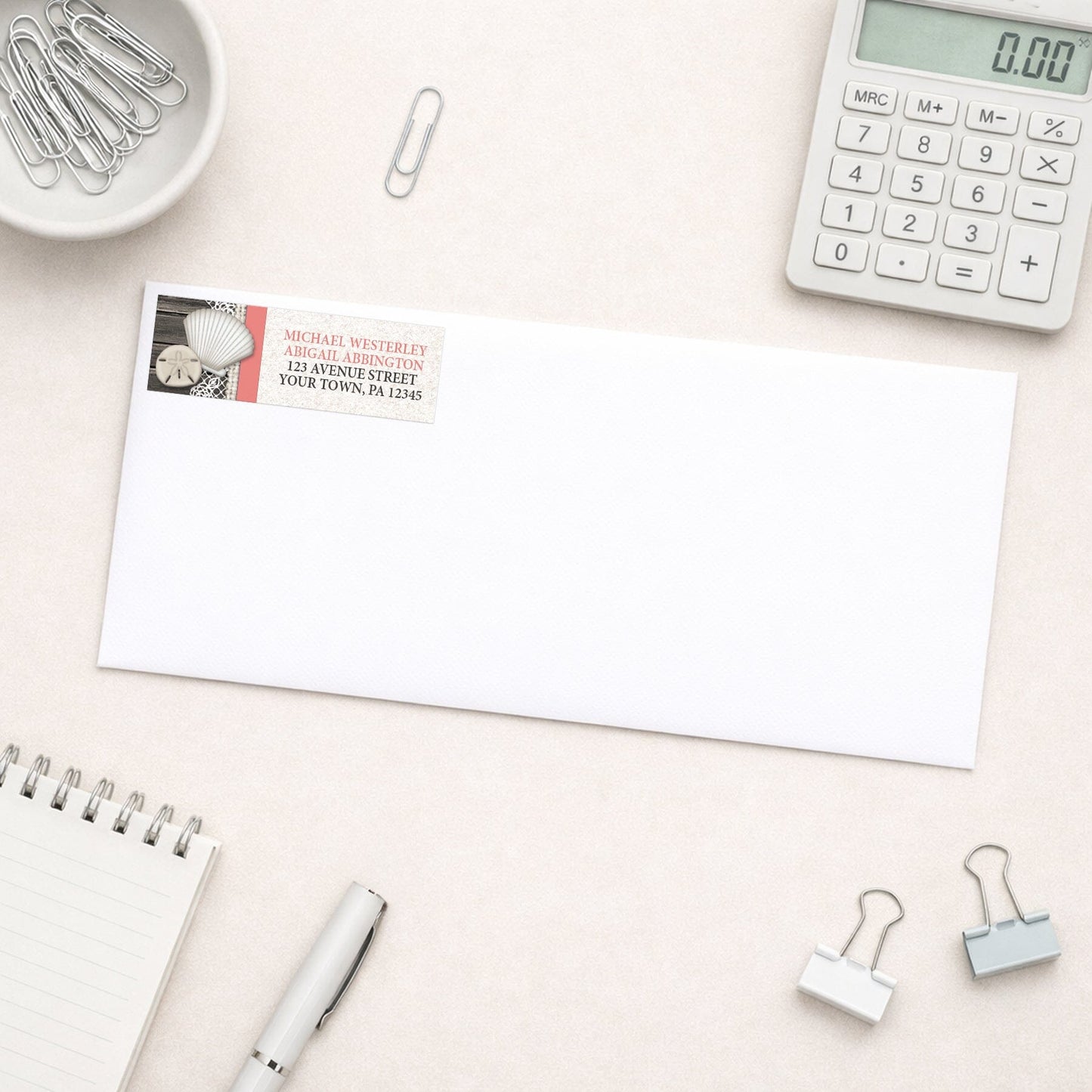 Seashell Lace Wood and Sand Coral Beach Address Label shown on a white envelope with everyday office supplies