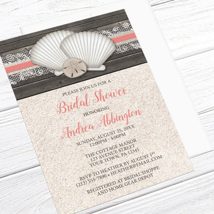 Beach bridal shower invitation with seashells and lace, wood, and sand, displayed at an angle with a white envelope on a white wood surface