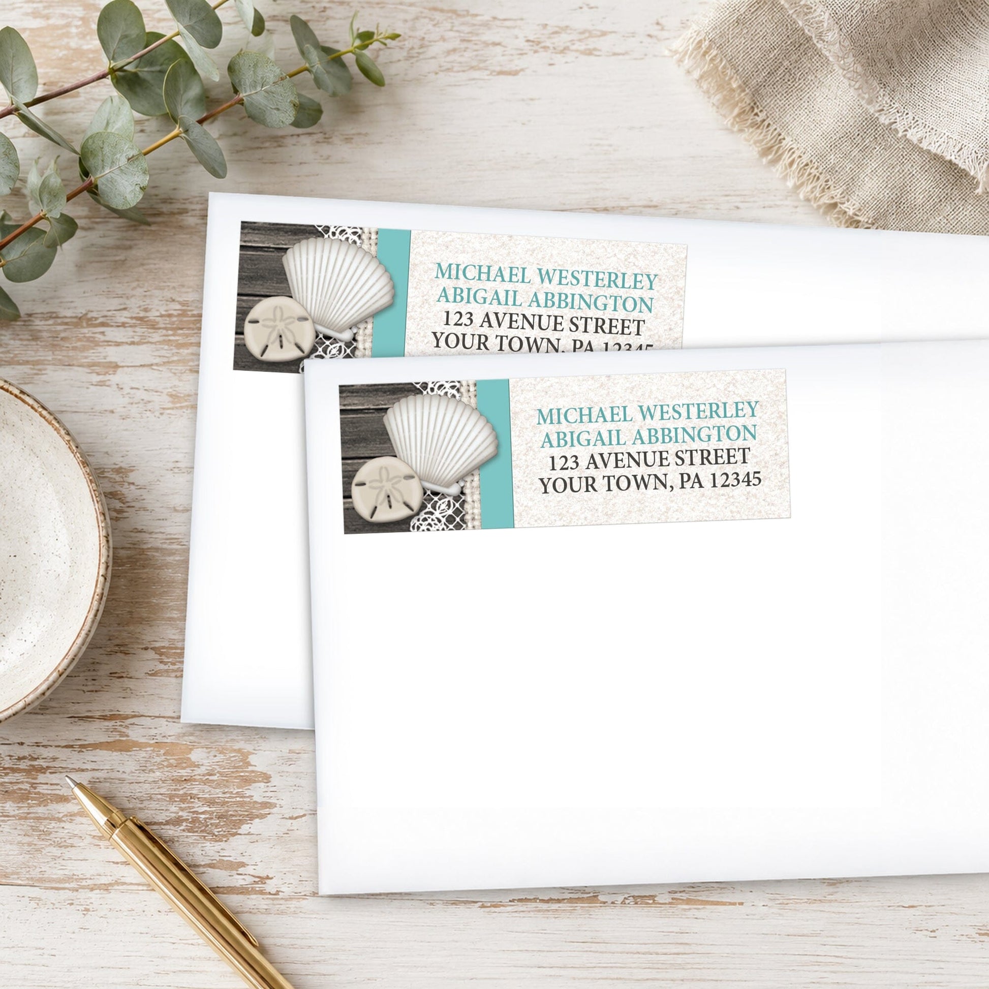 Seashell Lace Wood and Sand Teal Beach Address Labels on white envelopes shown on a wooden surface with eucalyptus leaves and a pen.