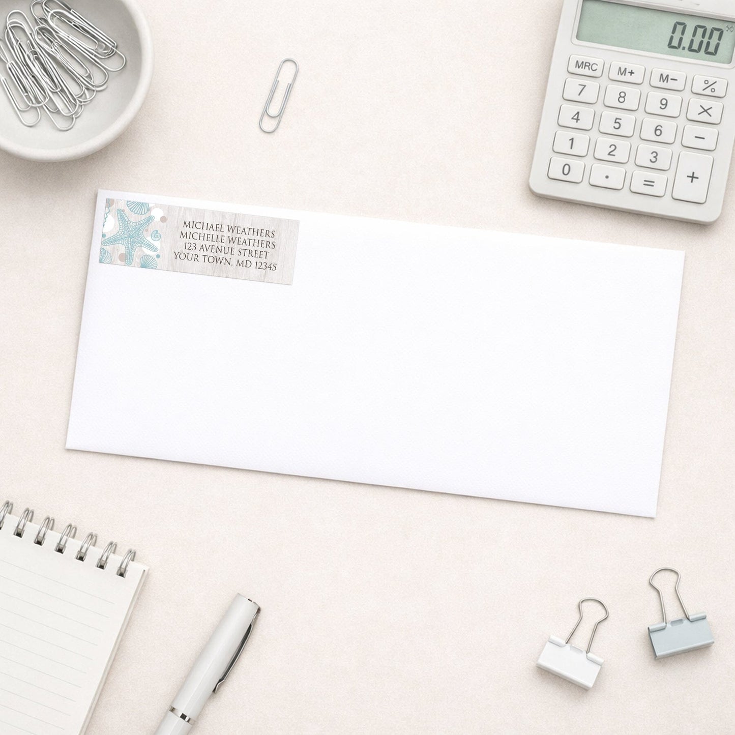 Seashell Whitewashed Wood Beach Address Label shown on a white envelope with everyday office supplies