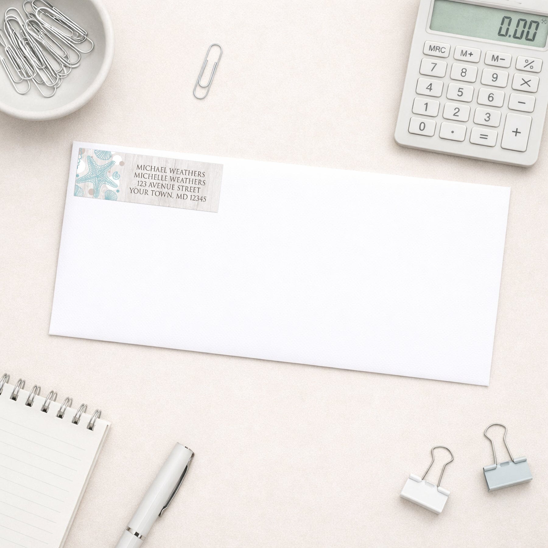 Seashell Whitewashed Wood Beach Address Label shown on a white envelope with everyday office supplies