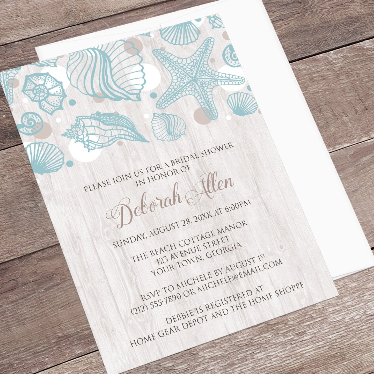 Seashell Whitewashed Wood Beach Bridal Shower Invitation shown at an angle on a rustic wood surface with a white envelope.
