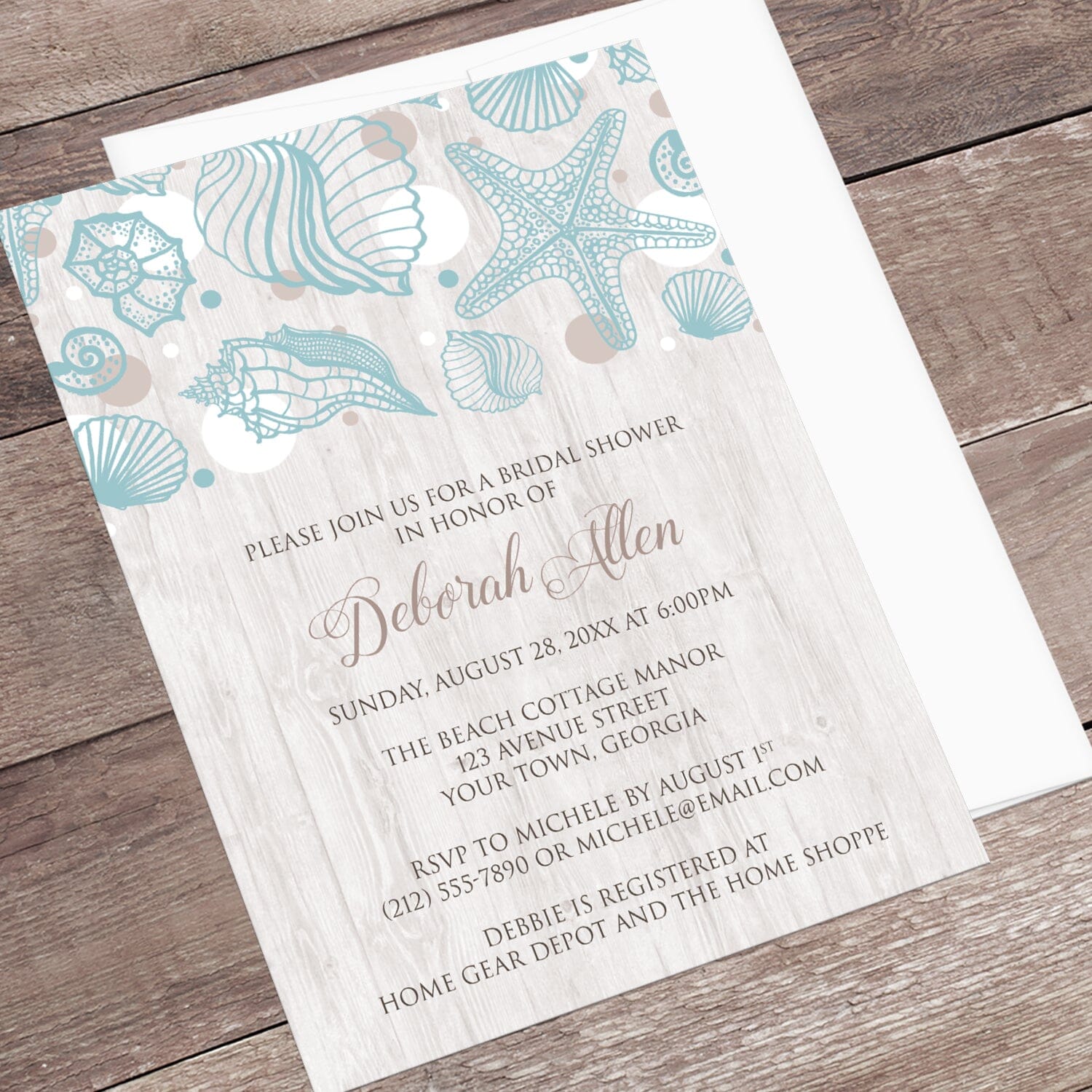 Seashell Whitewashed Wood Beach Bridal Shower Invitation shown at an angle on a rustic wood surface with a white envelope.