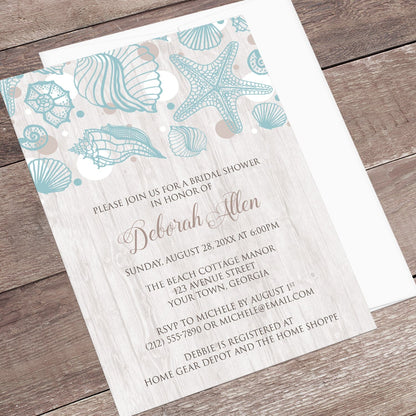 Seashell Whitewashed Wood Beach Bridal Shower Invitation shown at an angle on a rustic wood surface with a white envelope.