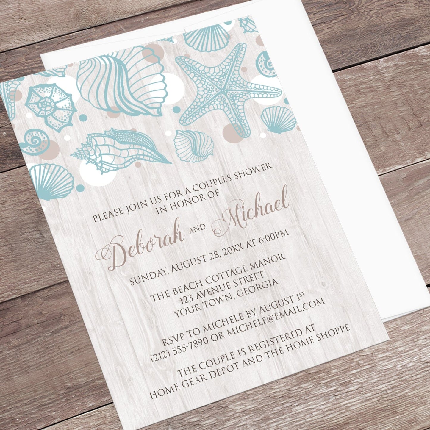 Seashell Whitewashed Wood Beach Couples Shower Invitation shown at an angle on a brown wood surface with a white envelope.