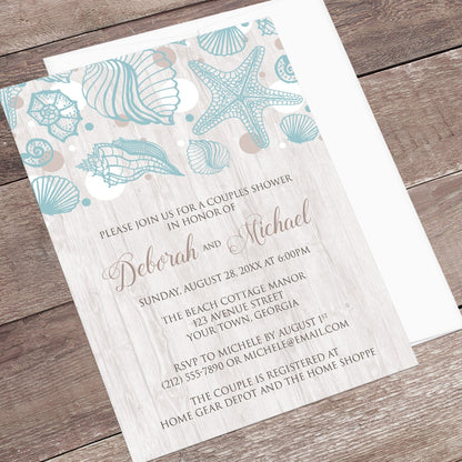 Seashell Whitewashed Wood Beach Couples Shower Invitation shown at an angle on a brown wood surface with a white envelope.