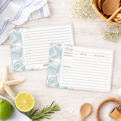 Set of Seashell Whitewashed Wood Beach Recipe Cards on a beach house wooden surface with kitchen items.