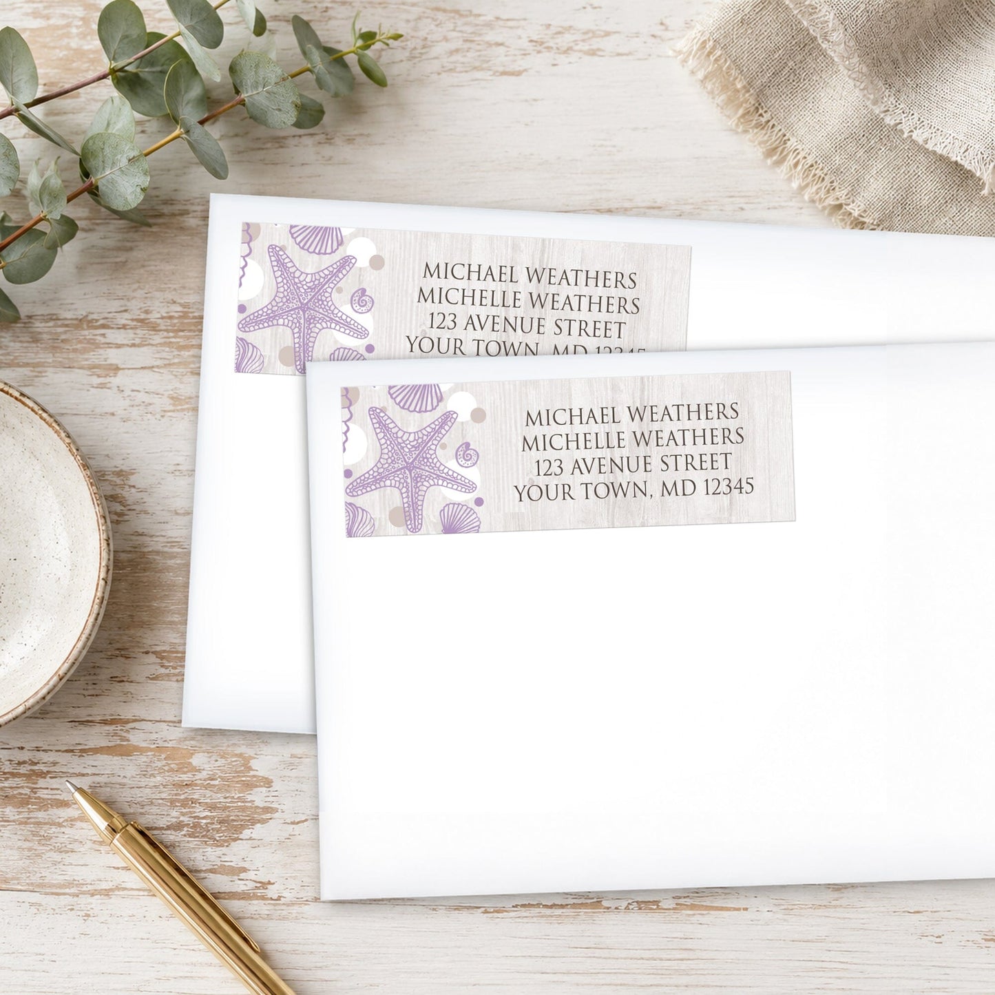 Seashell Whitewashed Wood Purple Beach Address Labels, shown on white envelopes, on a wooden surface with eucalyptus leaves and a pen.