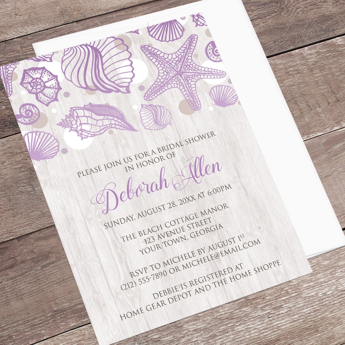Seashell Whitewashed Wood Purple Beach Bridal Shower Invitation shown at an angle on a wooden surface with a white envelope.