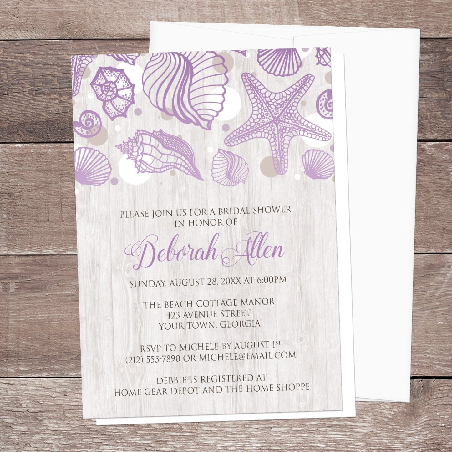 Seashell Whitewashed Wood Purple Beach Bridal Shower Invitation shown on a wooden surface with a white envelope.