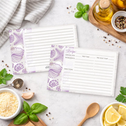 Set of Seashell Whitewashed Wood Purple Beach Recipe Cards on a kitchen counter with ingredients and utensils.