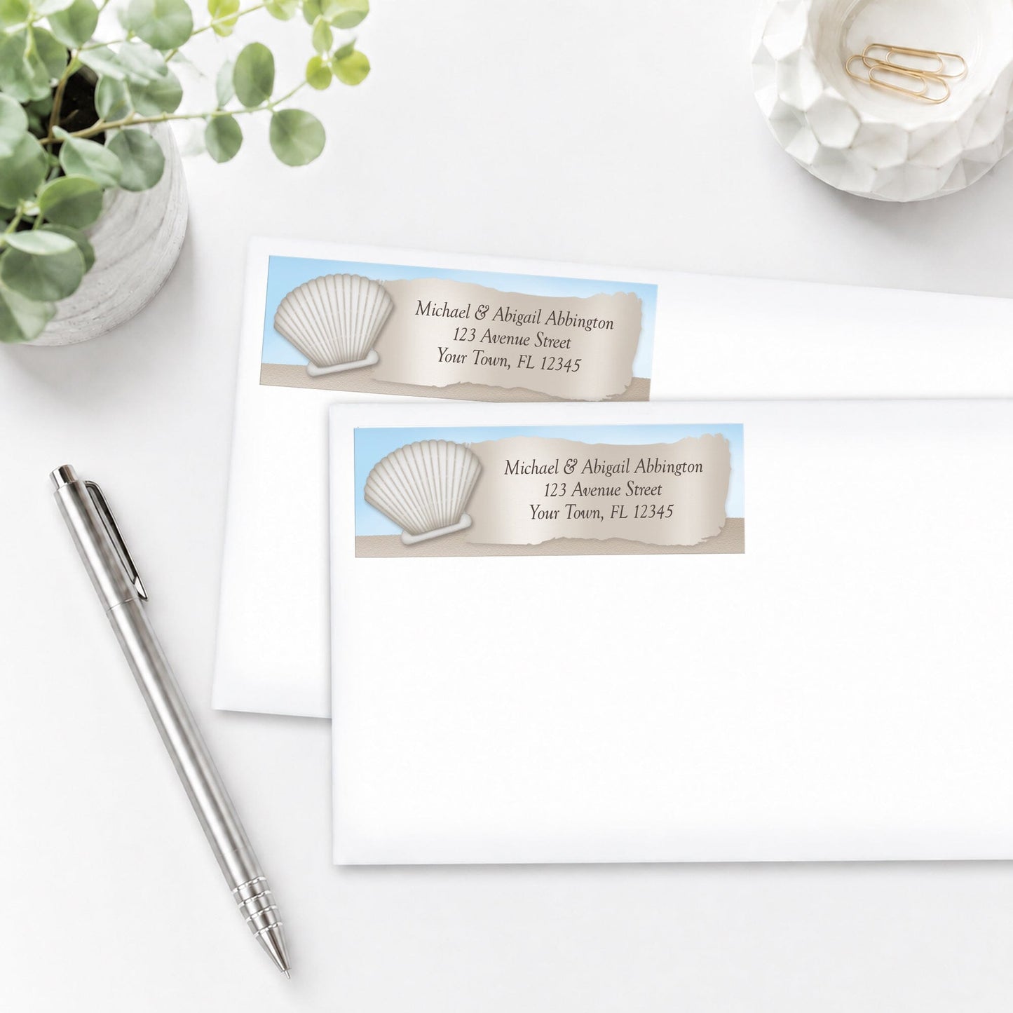 Seashell in the Sand Beach Address Labels on white envelopes, shown on a white surface with a pen and plant.