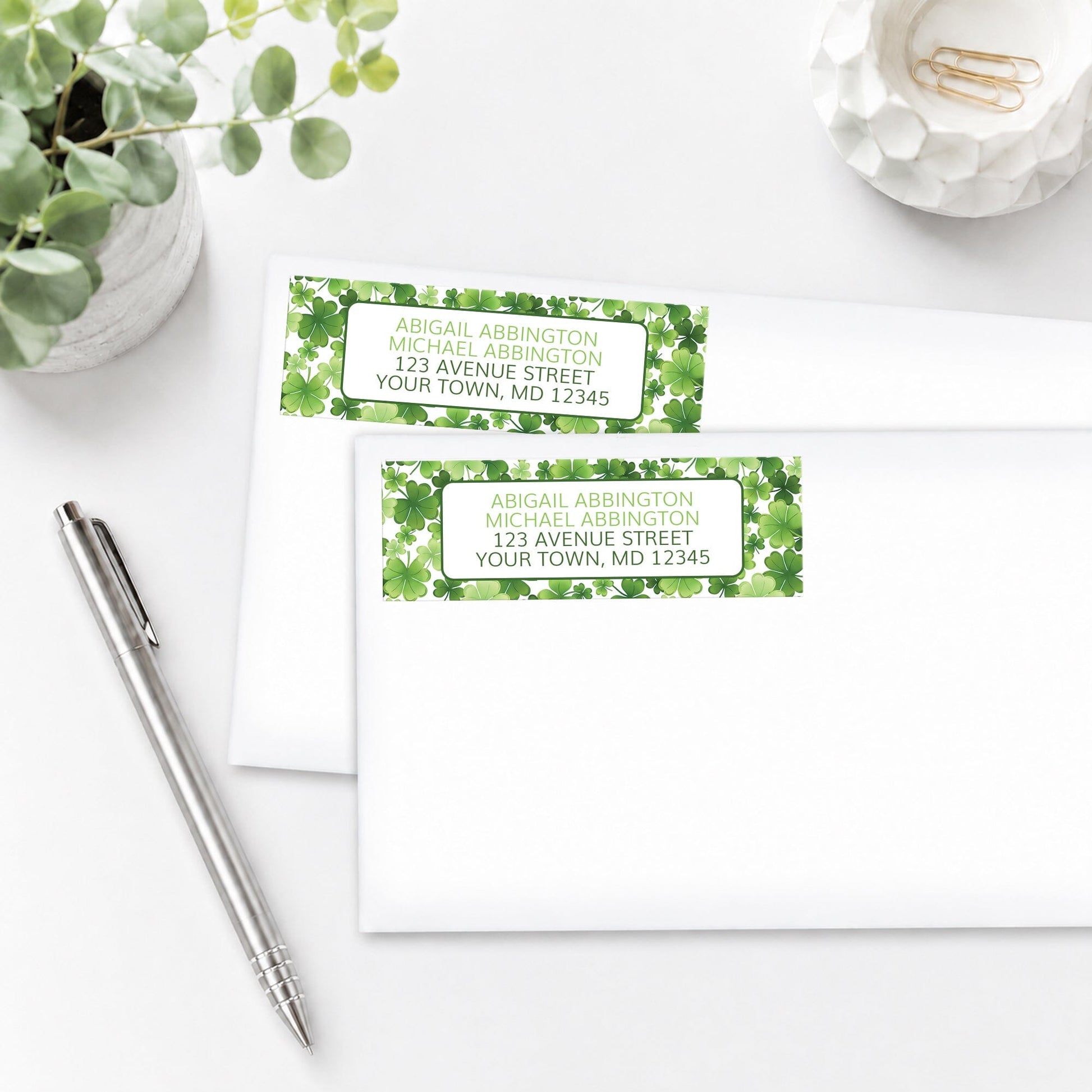 Address labels with shamrock design, shown on white envelopes, on a white surface with a pen and plant.