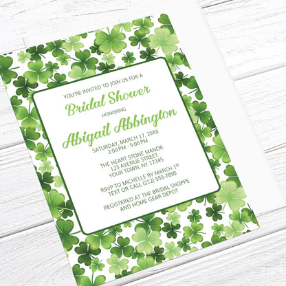 Bridal shower invitation with green shamrock pattern, displayed at an angle with a white envelope on a white wood surface