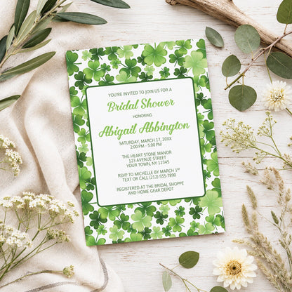 Shamrocks and 4-Leaf Clovers Bridal Shower Invitation shown on a light wooden surface with spring and summer plants.