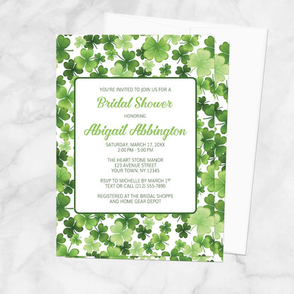 Bridal shower invitation with green shamrock pattern, displayed with a white envelope on a marble surface