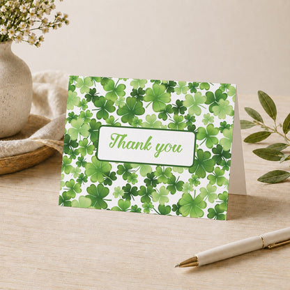 Shamrocks and 4-Leaf Clovers Thank You Card shown on a tabletop with a vase, plants, and a pen.