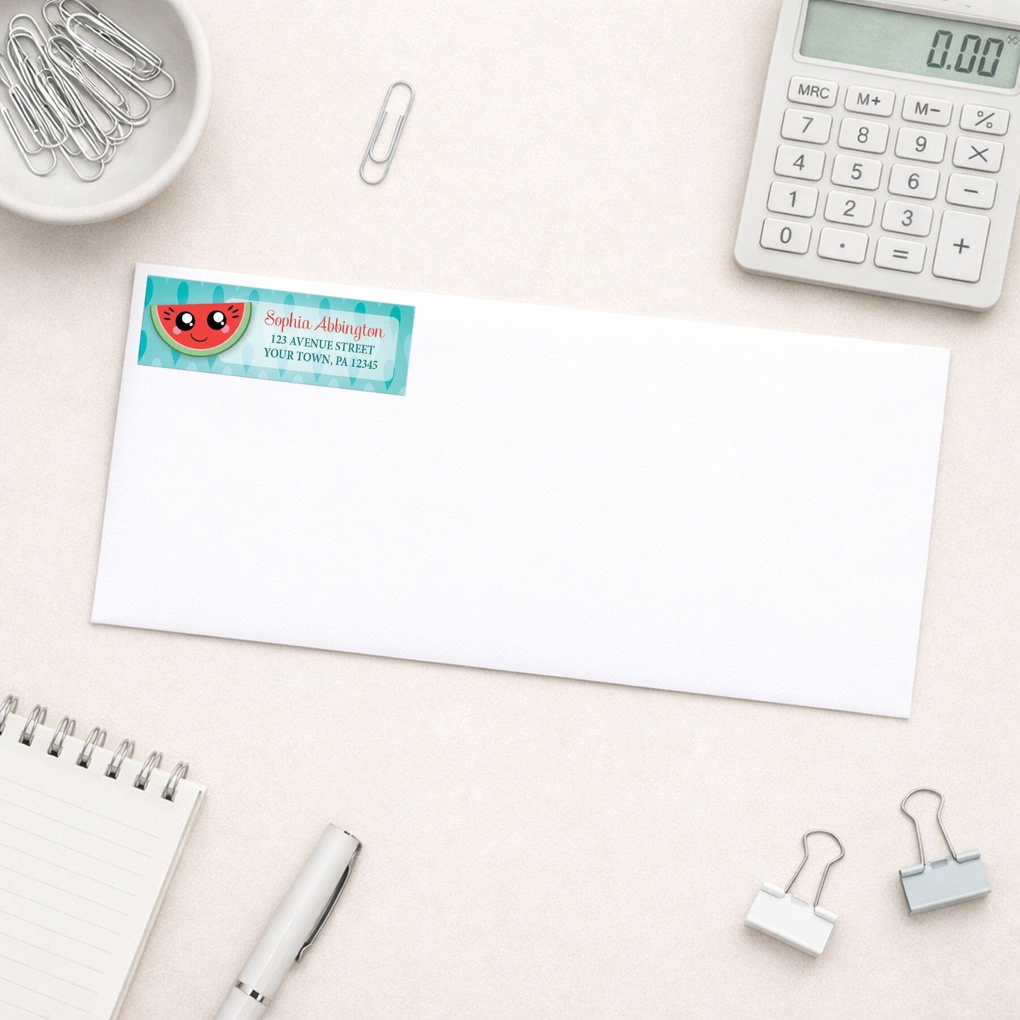 Smiling Watermelon Slice Address Label shown on a white envelope with everyday office supplies