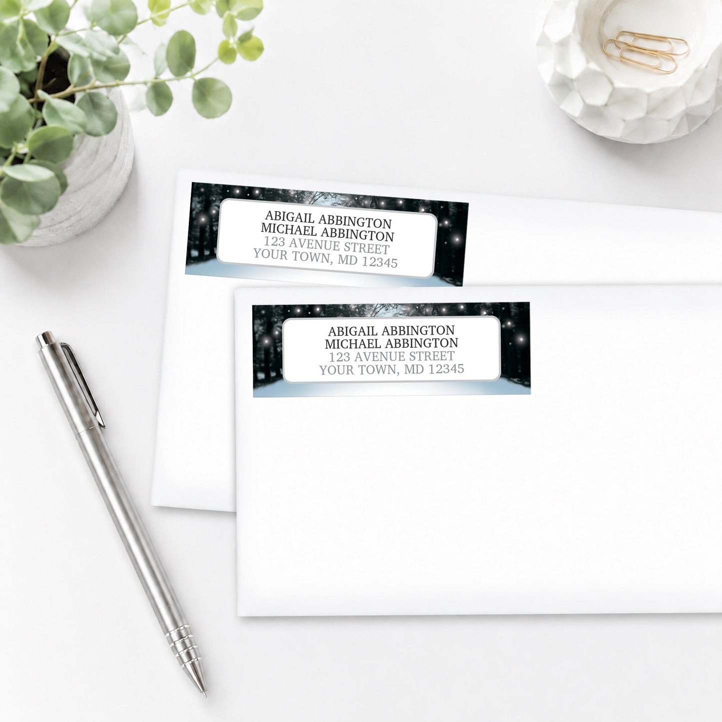 Address labels with winter scene design on a white surface with a pen and plant.