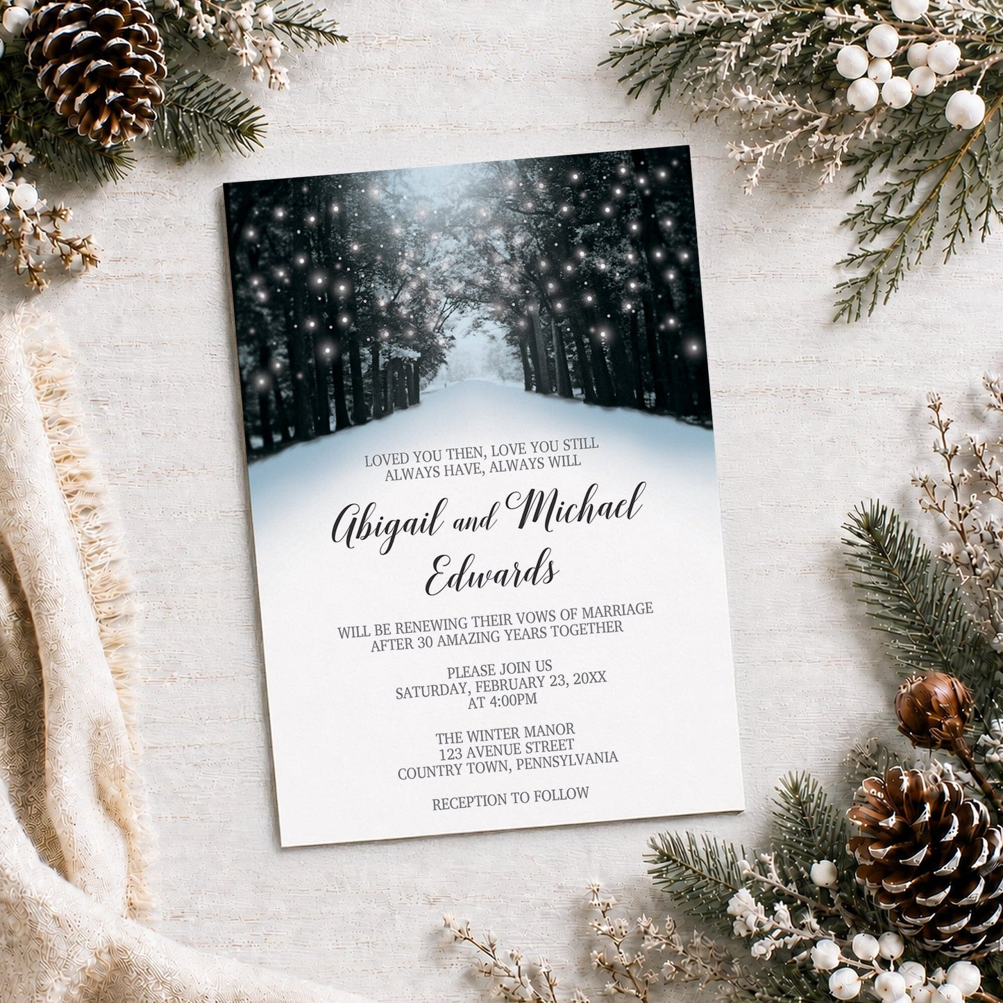 Snowy Winter Road Tree Lights Vow Renewal Invitation shown on a light surface with winter greenery, a blanket, and pine cones.