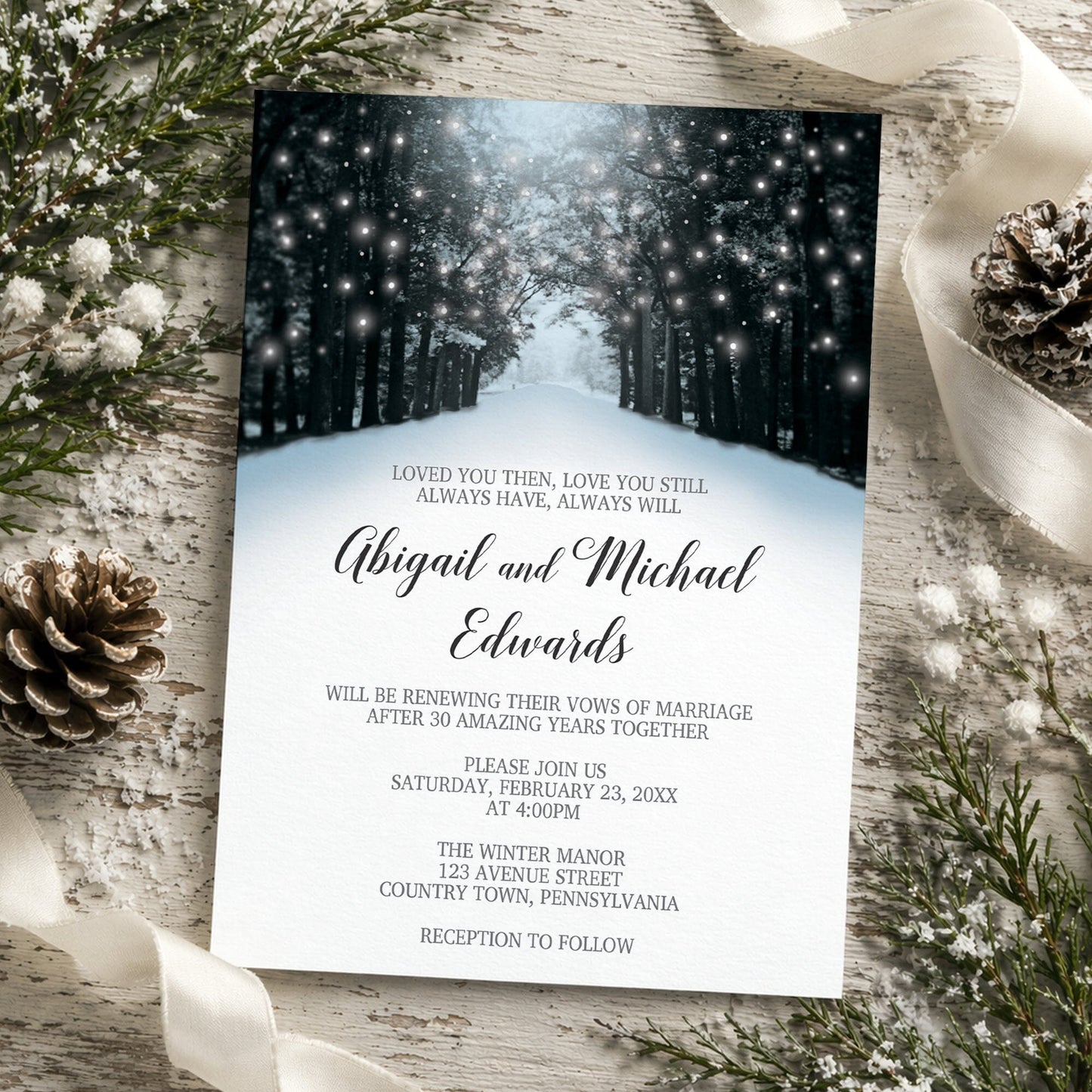 Snowy Winter Road Tree Lights Vow Renewal Invitation shown on a rustic wooden surface with winter greenery, ribbon, and pine cones.