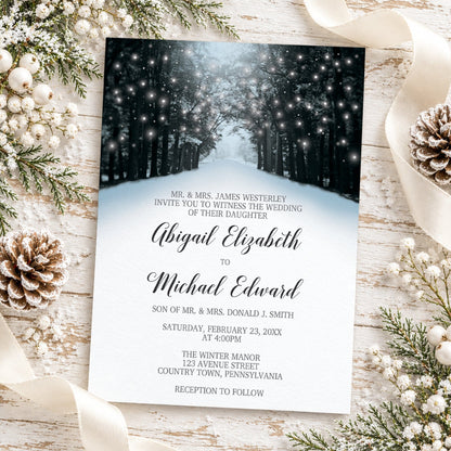 Winter wedding invitation with snowy tree-lined road, glowing white lights among dark woodland trees, black script names, and gray wedding details, styled in a flat lay with winter pine branches, white berries, a pinecone, and a cream ribbon on a whitewashed wood background.