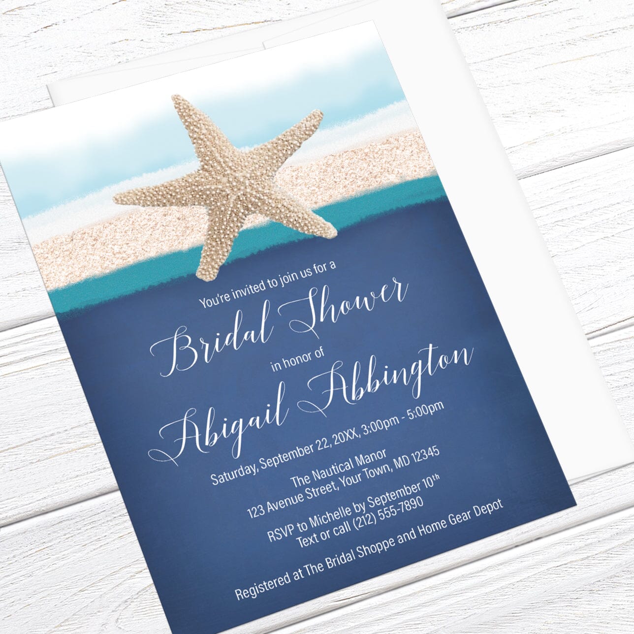Beach bridal shower invitation with a starfish over sand, blue, and teal stripes, over a blue background for your personalization details in white, displayed at an angle with a white envelope on a white wood surface