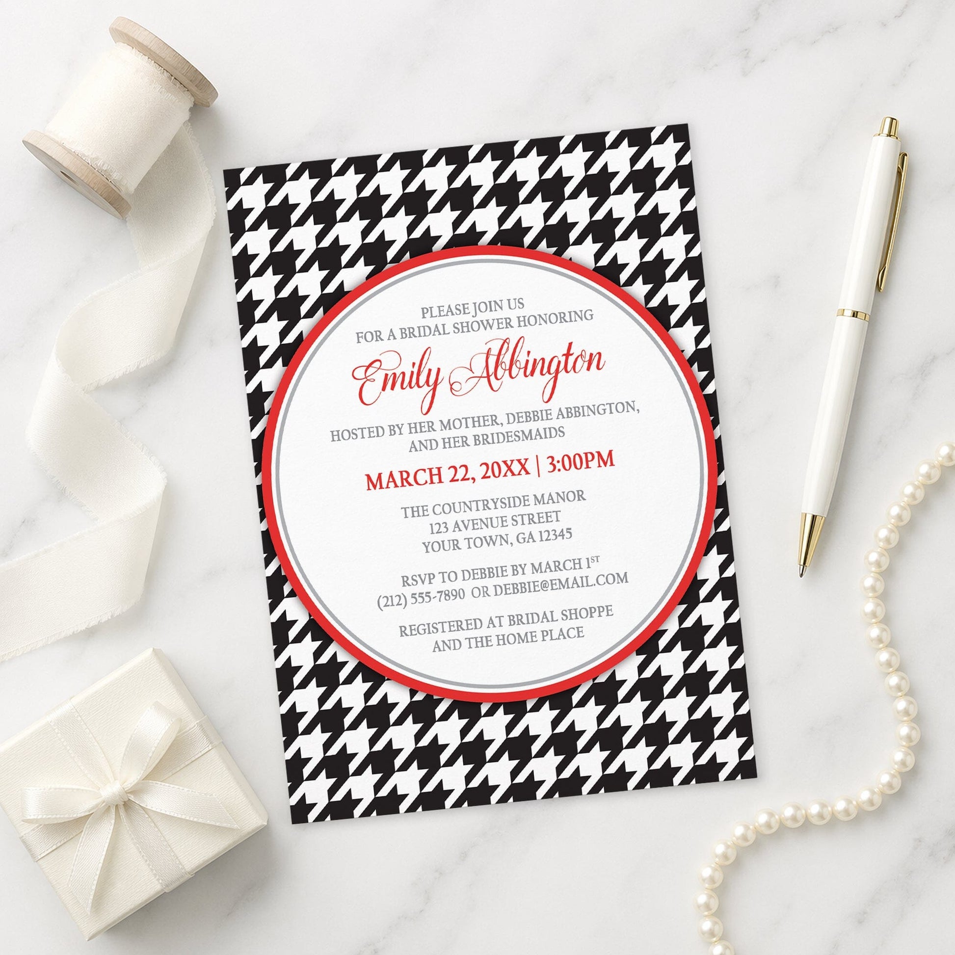 Stylish Black Houndstooth Red Bridal Shower Invitation shown on a marble surface with a white gift box, pen, ribbon, and pearls.