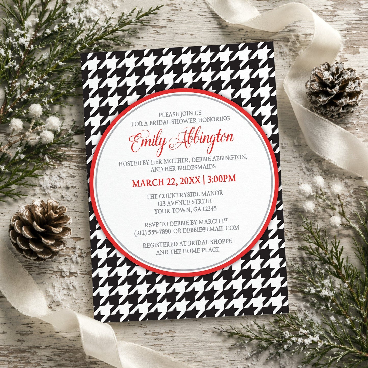 Stylish Black Houndstooth Red Bridal Shower Invitation shown on a rustic wooden surface with winter greenery, pine cones, and ribbons.