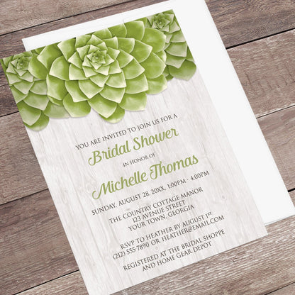 Bridal shower invitation with green succulent design shown at an angle on a wooden surface with a white envelope.