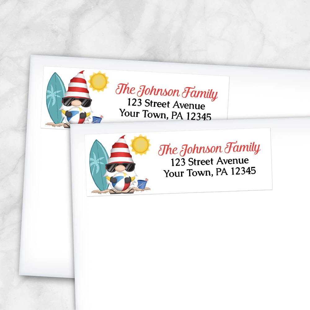 Summer Beach Gnome Address Labels at Artistically Invited. Example of labels on envelopes. These address labels are designed with an illustration of a cute gnome holding a beach ball with a surfboard and a bucket in the sand, and a sun above. Your personalized return address is custom printed in red and black over white to the right of the beach-themed gnome.