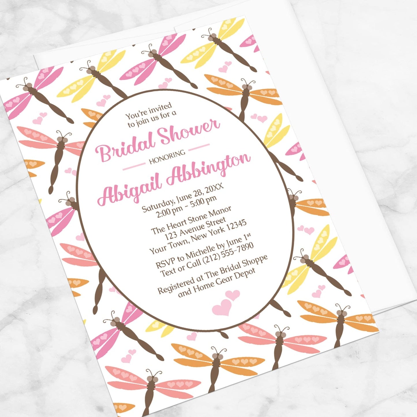 Summer Dragonfly Bridal Shower Invitation shown at an angle on a marble surface with a white envelope.