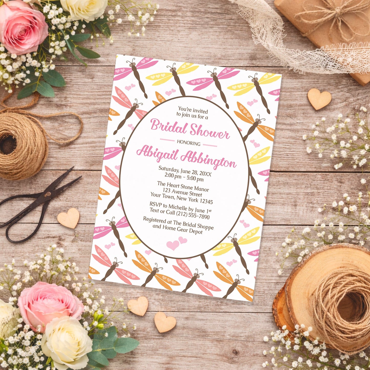 Summer Dragonfly Bridal Shower Invitation shown on a wooden surface with spring and summer flowers, small wood hearts, and twine.
