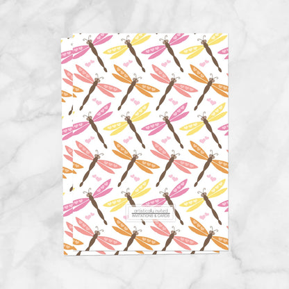 The back side of the Summer Dragonfly Bridal Shower Invitation, displaying the dragonfly pattern design and store logo, shown on a marble surface.