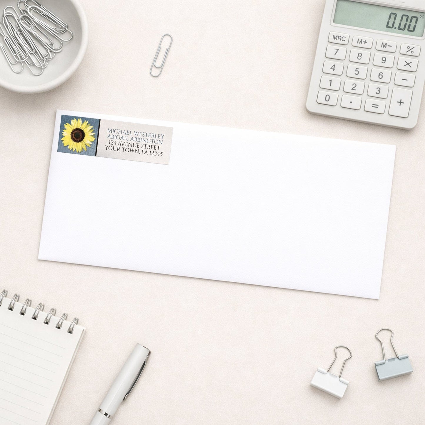 Sunflower and Blue Rustic Address Label shown on a white envelope with everyday office supplies