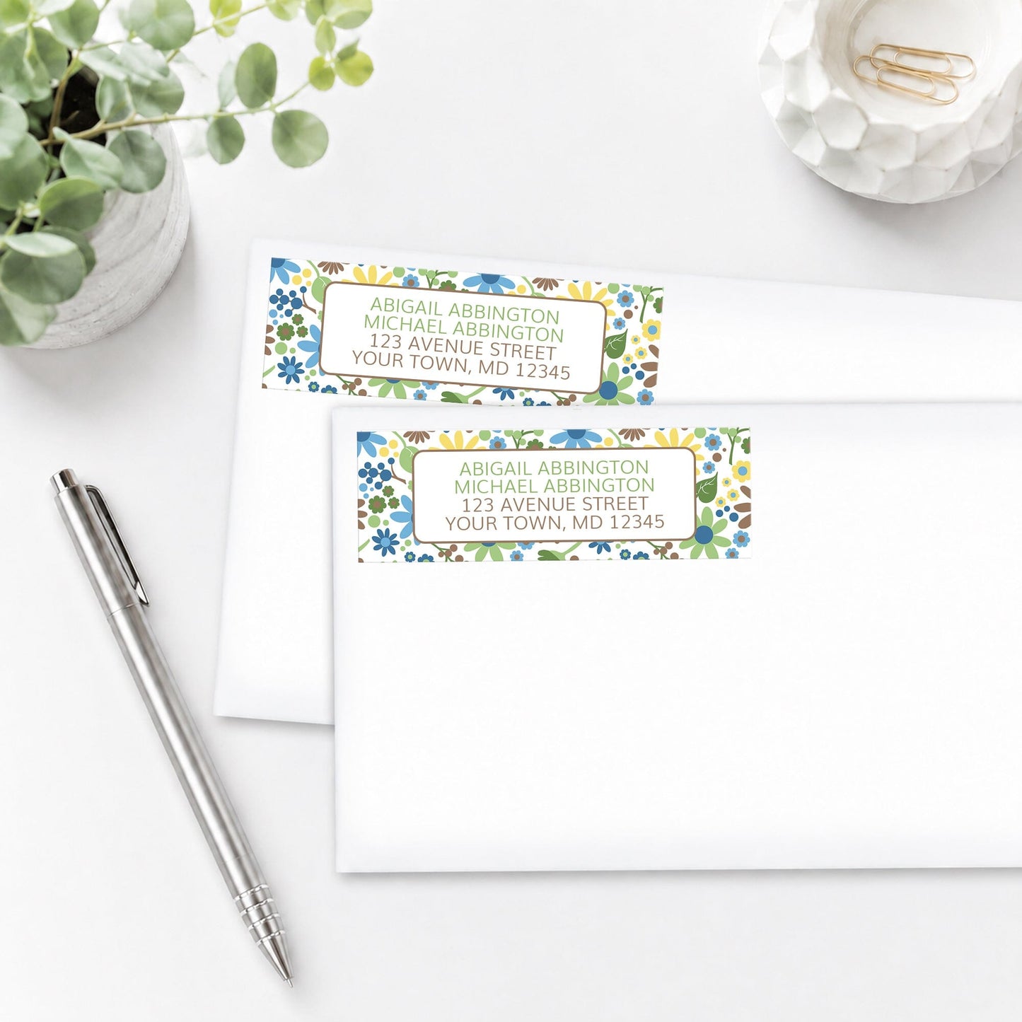 Sunny Summer Flowers Address Labels shown on white envelopes, on a white surface with a plant and a pen.