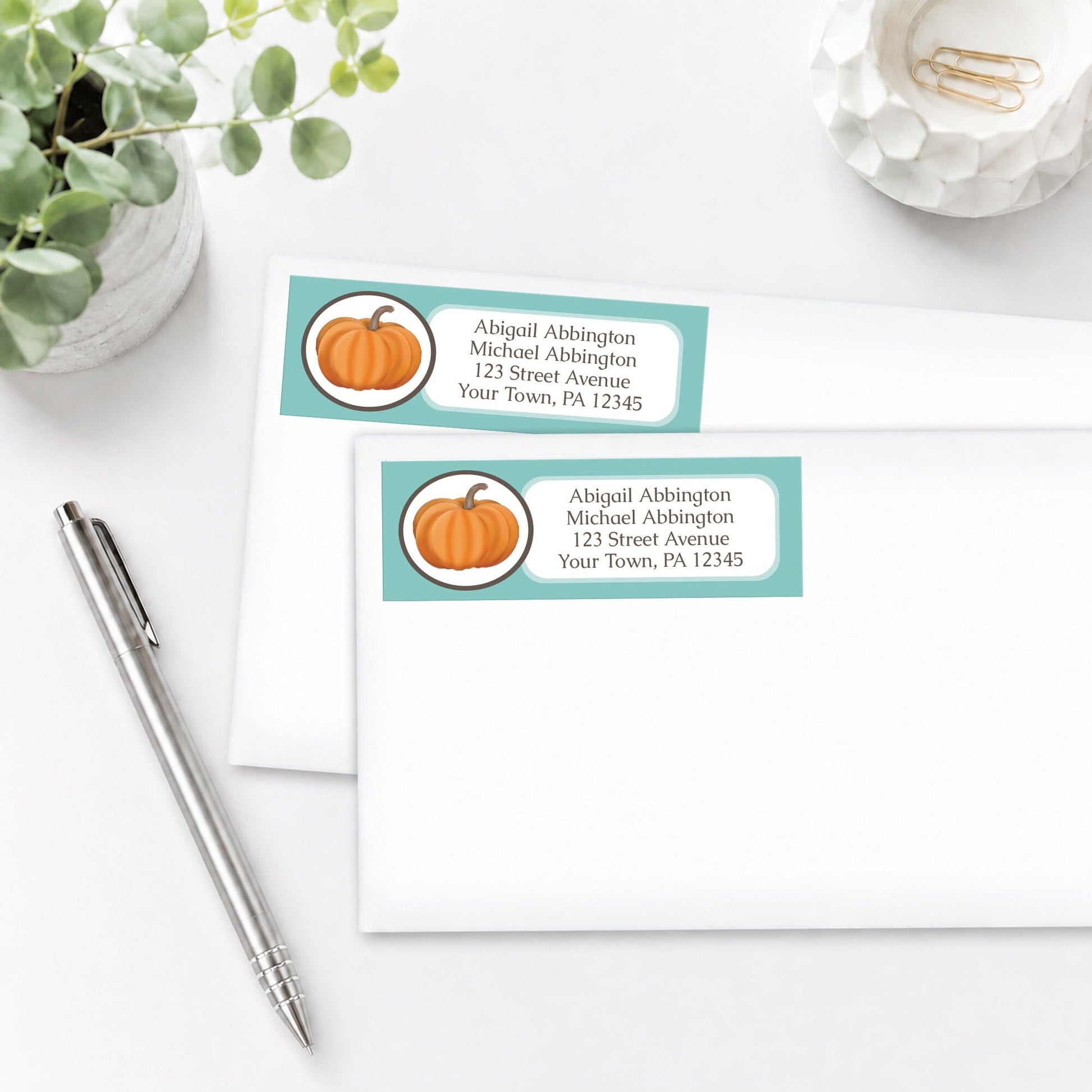 Teal Pumpkin Address Labels on envelopes with a pen and plant beside them.