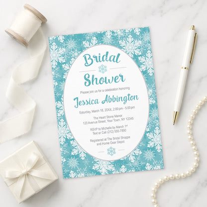 Teal Snowflake Bridal Shower Invitation shown on a marble surface with a white gift box, pen, ribbon, and pearls.