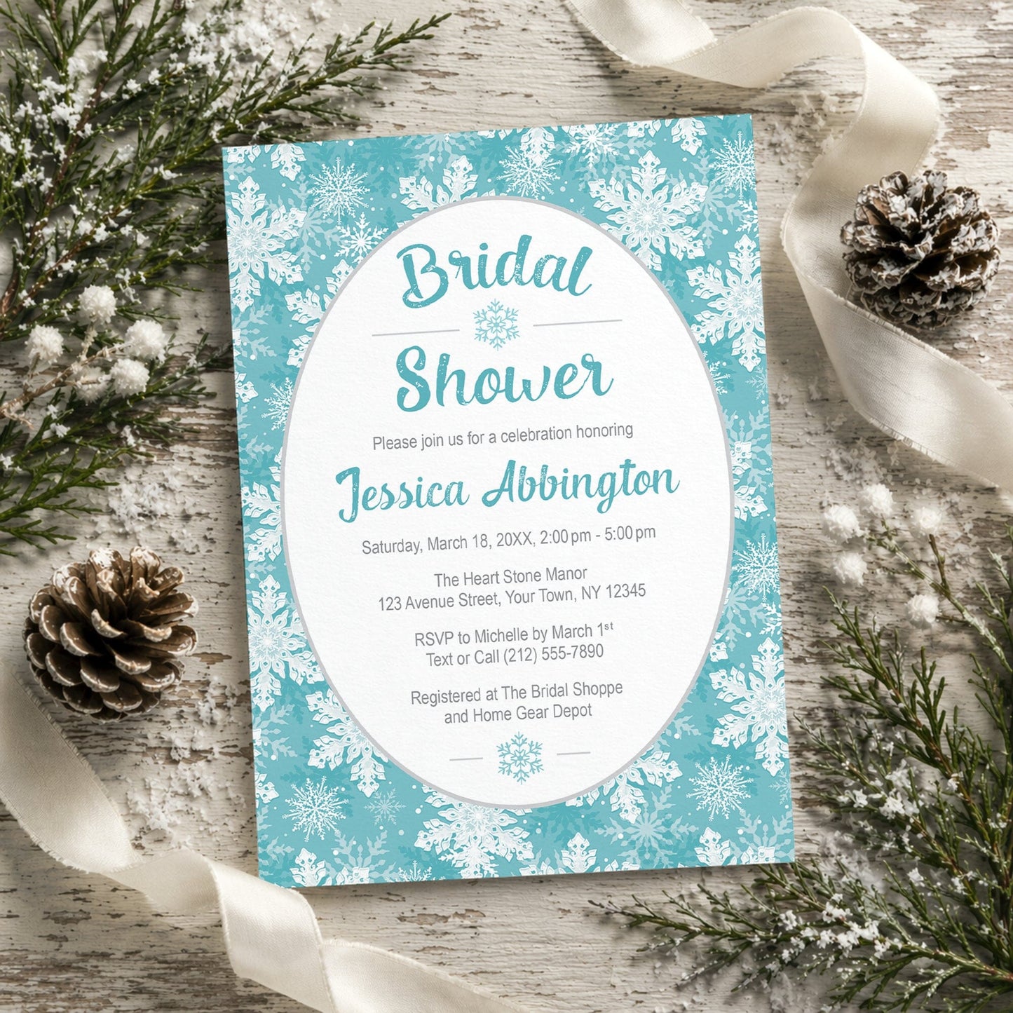 Teal Snowflake Bridal Shower Invitation shown on a rustic wooden surface with winter greenery, pine cones, and ribbons.