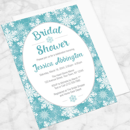 Teal Snowflake Bridal Shower Invitation shown at an angle on a marble surface with a white envelope.