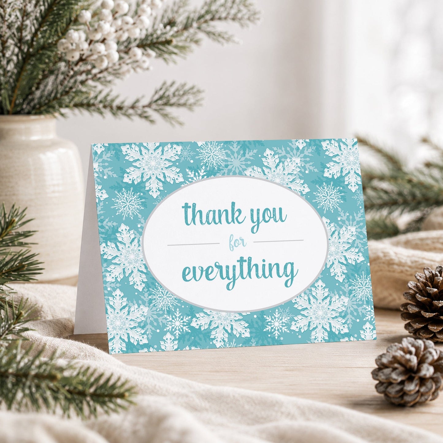 Teal Snowflake Winter Thank You Card shown on a tabletop with a vase, winter greenery, and pine cones.