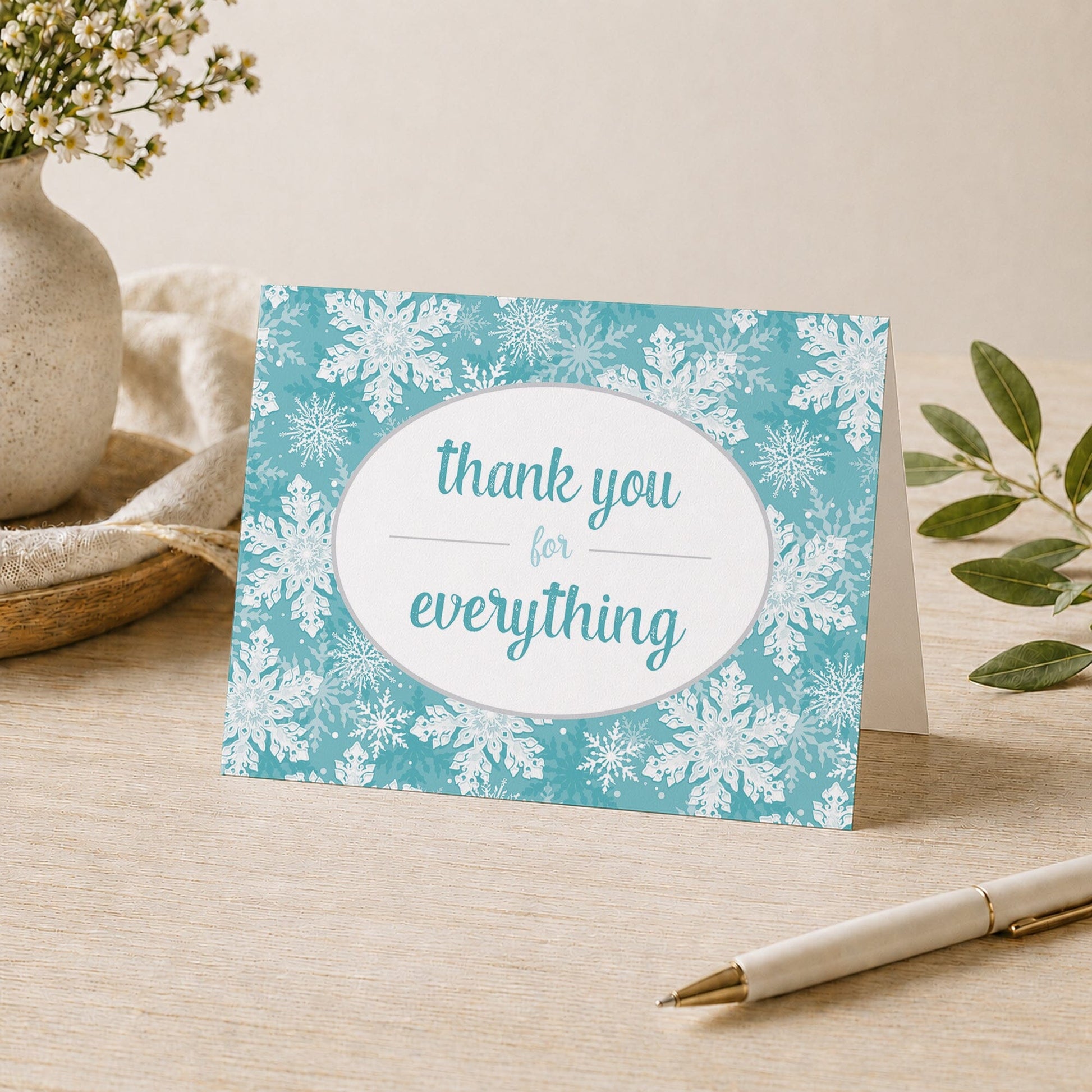 Teal Snowflake Winter Thank You Card shown on a desk with a vase, plants, and a pen.