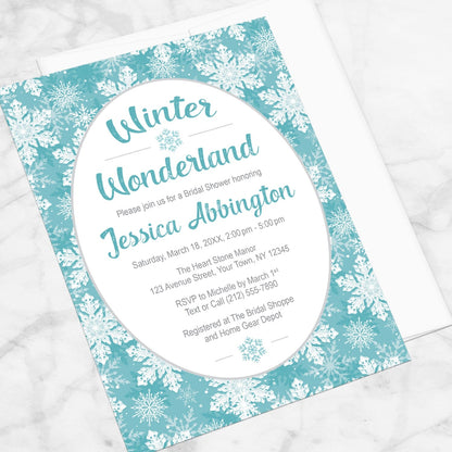 Teal Snowflake Winter Wonderland Bridal Shower Invitation shown at an angle on a marble surface with a white envelope.