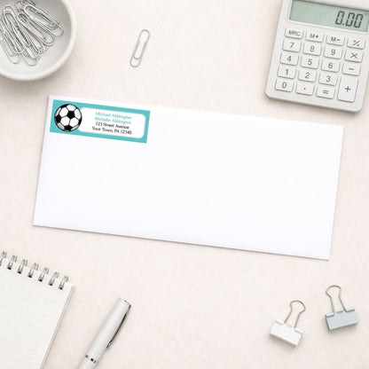 Teal Soccer Ball Return Address Label shown on a white envelope with everyday office supplies