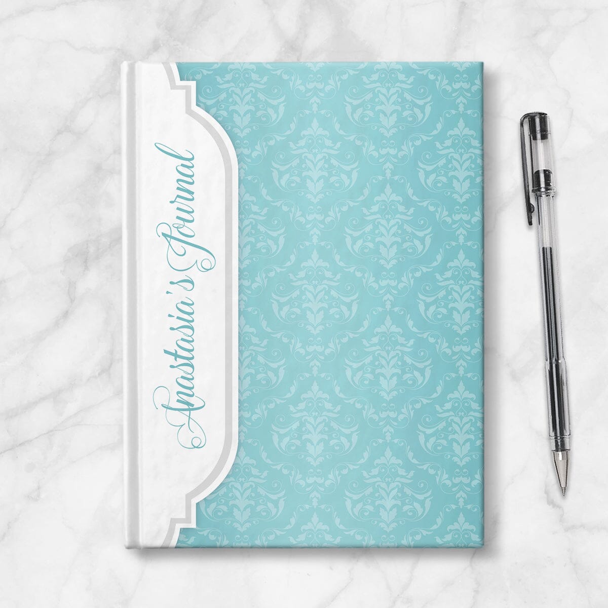 Personalized Turquoise Damask Journal at Artistically Invited. Image shows the book on a countertop next to a pen.
