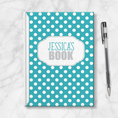 Personalized Turquoise Polka Dot Journal at Artistically Invited. Image shows the book on a countertop next to a pen.