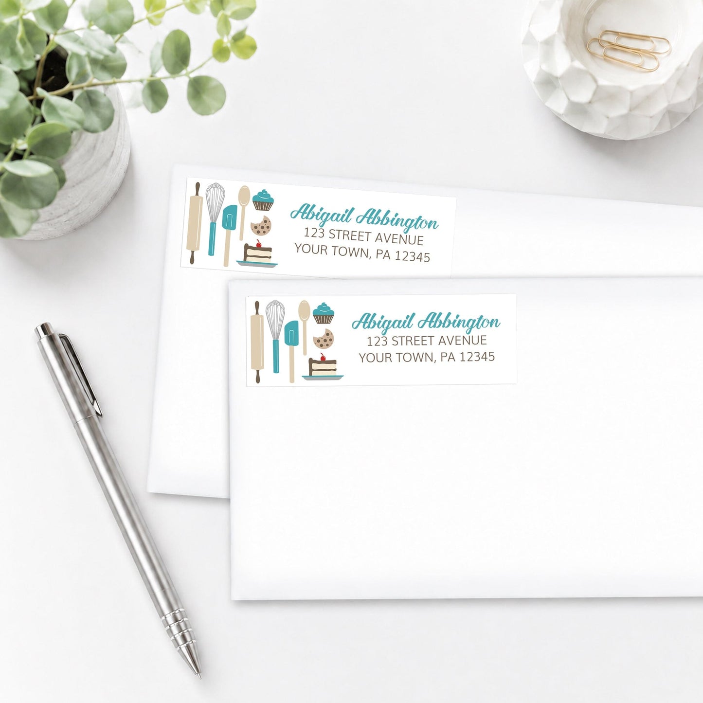 Turquoise Baking Address Labels shown on white envelopes, on a white surface with a plant and a pen.