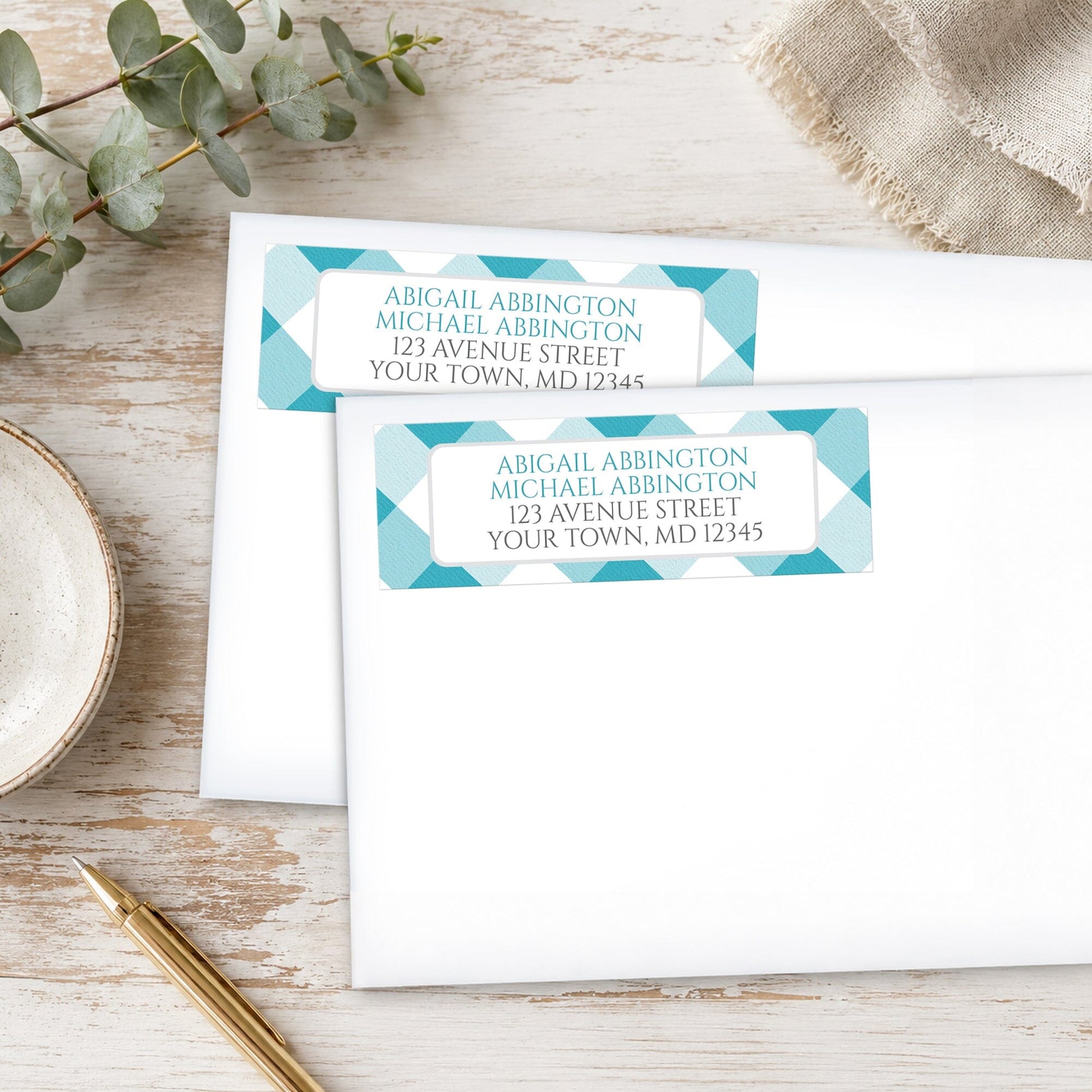 Turquoise Gingham Address Labels with a classic check pattern, shown on white envelopes, on a wooden surface with eucalyptus leaves and a pen.