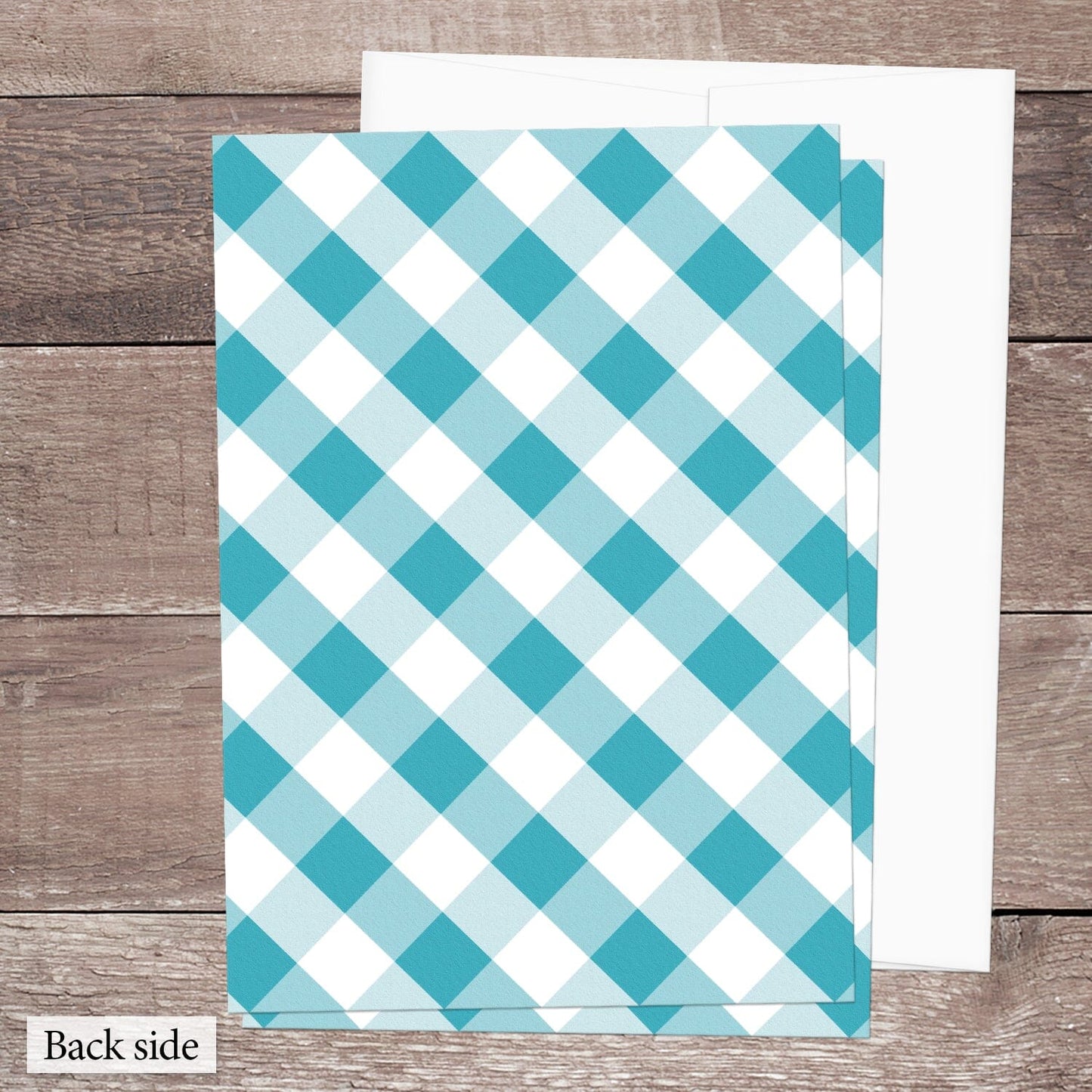 The back side of the Turquoise Gingham Vow Renewal Invitation shown on a brown wood surface with a white envelope.